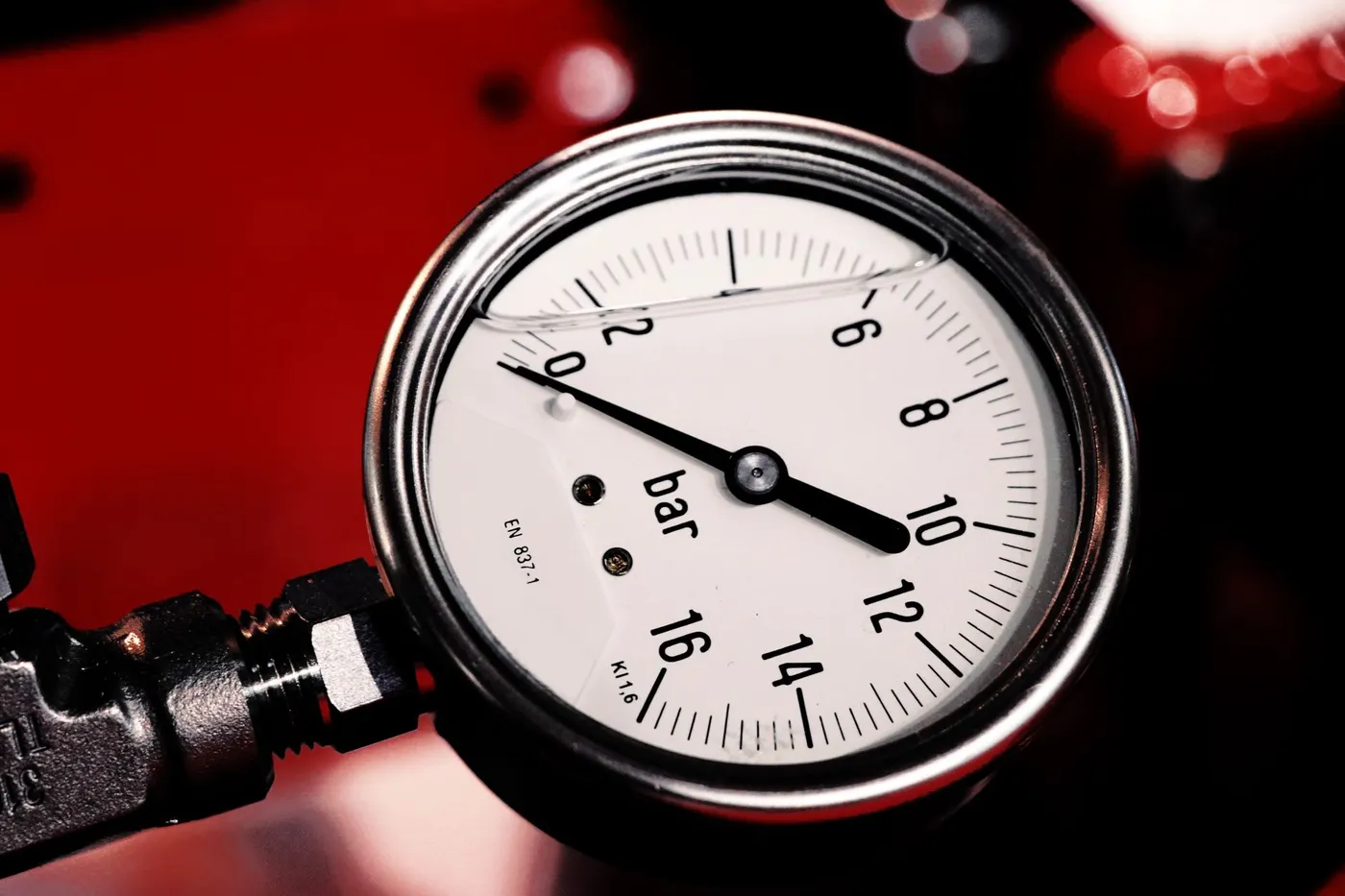 Round pressure gauge marked in bar on a 0 to 16 scale, with the needle pointing at 10 bar, fitted to a black pipe connection