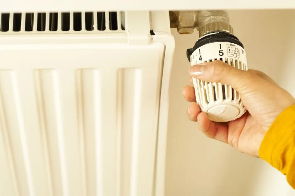 Hand turning the thermostatic valve head on a white panel radiator