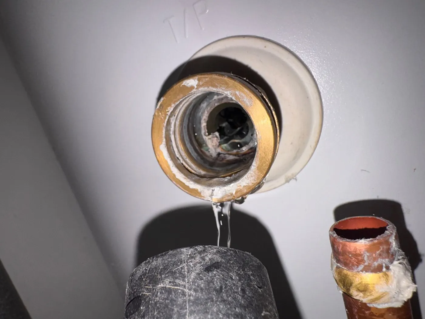 Water dripping from the open port of a pressure relief fitting on an unvented cylinder, above a section of copper pipe