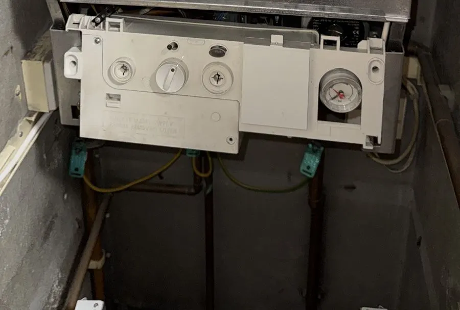 Wall-mounted boiler with its front panel open, showing the pressure gauge on the right and the copper pipework running down from the underside of the boiler